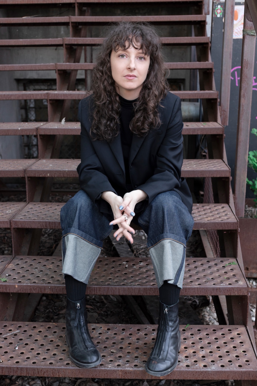 Andra Ionel sitting on rusted steel stairs, hands folded, looking calmly at the camera.